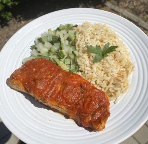 Fish with red sauce, brown rice, and vegetables on a white plate.